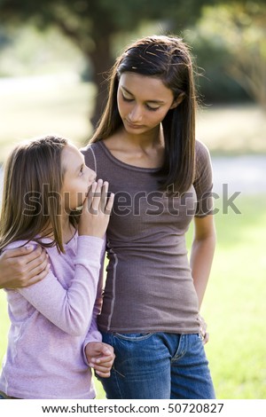 Ten year old girl whispering to her older teenage sister while walking outdoors