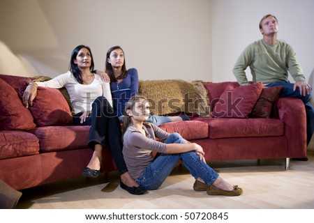 Interracial family of four sitting together on living room sofa watching television