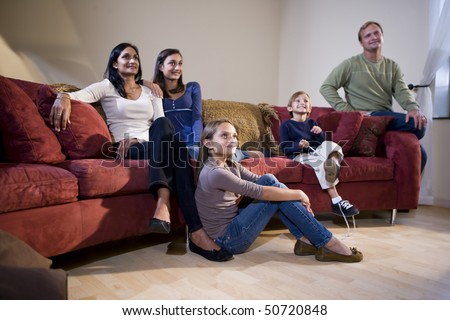 Interracial family of five sitting together on living room sofa watching television