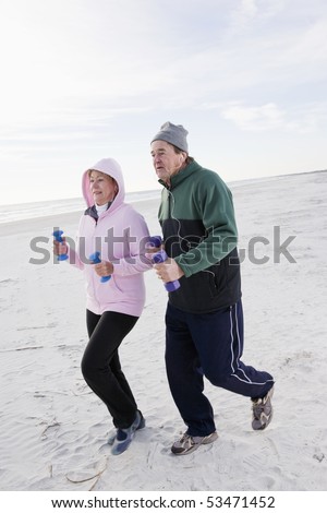 Senior couple exercising, jogging on beach with hand weights