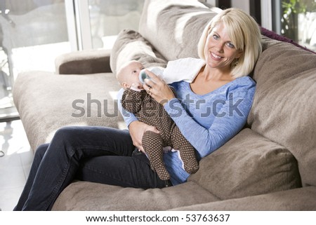 Mom feeding bottle to 3 month old baby at home on couch