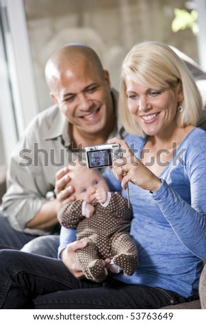 Parents with 3 month old baby on lap at home, mom holding camera