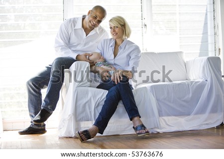 Parents with sleeping 3 month old baby on sofa in sunny home