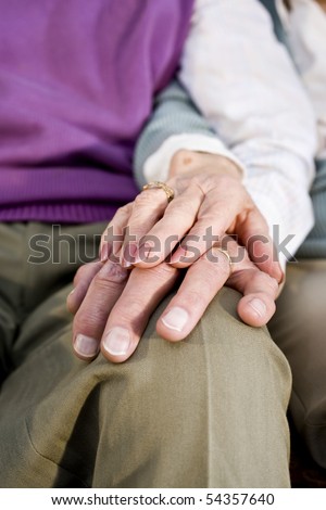 Close-up detail of hands of senior couple touching and resting on knee
