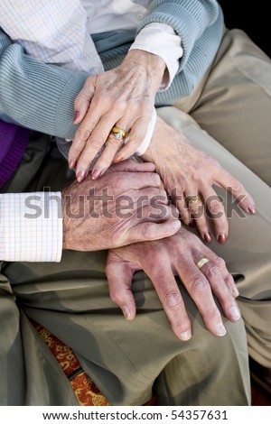 Close-up detail of hands of senior couple touching and resting on knees