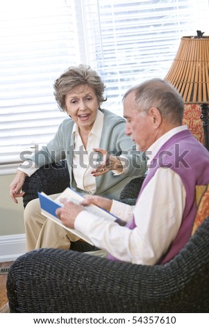 Senior couple chatting in living room reading book, focus on woman talking