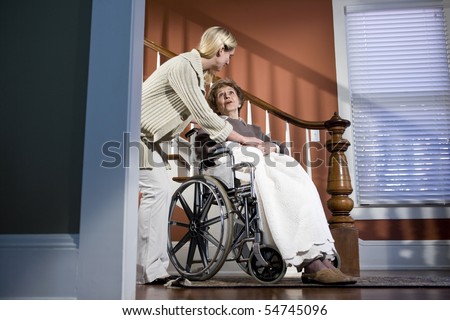 Female nurse helping elderly woman in wheelchair at home