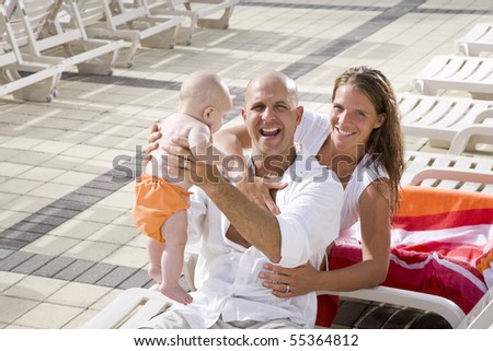 Young family on vacation, relaxing on pool deck lounge chairs