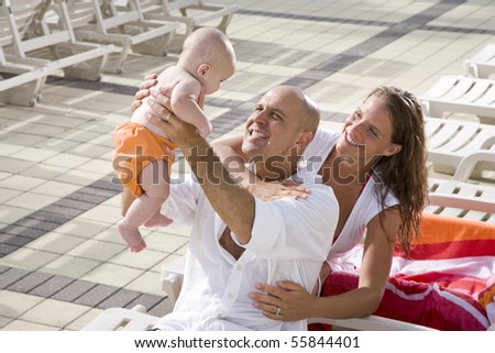 Young family on vacation, relaxing on pool deck lounge chairs