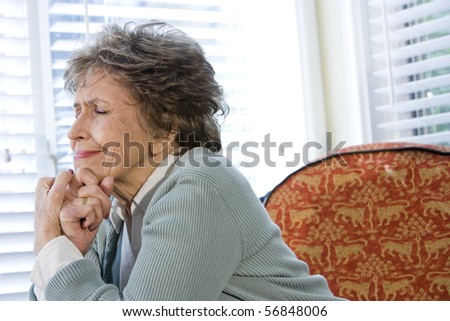 Elderly woman upset sitting alone by window with eyes shut
