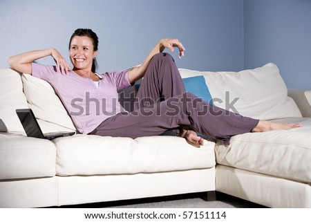 Happy mid-adult woman sitting on couch smiling with laptop