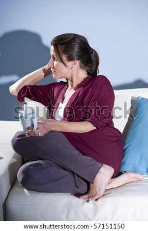 Pensive mid-adult woman drinking coffee thinking on couch at home