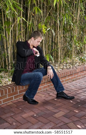 Young well-dressed man sitting on patio fixing handkerchief