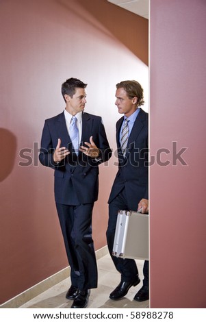 Two businessmen talking and walking down office corridor
