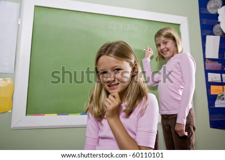 Back to school - 8 year old girls writing on blackboard in classroom, focus on foreground