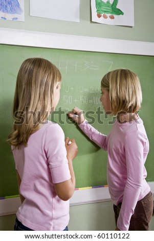 Back to school - 8 year old girls writing on blackboard in classroom, doing math