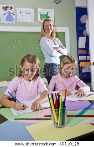 Back to school - 8 year old girls writing in notebooks in classroom with teacher watching