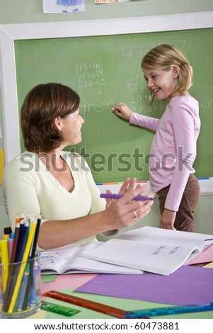 Back to school - 8 year old student and teacher by blackboard in classroom