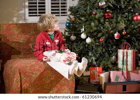 Little boy looking up at Christmas tree with present in lap