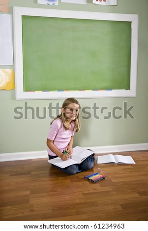 Back to school - girl writing in classroom by green blackboard, 8 years old