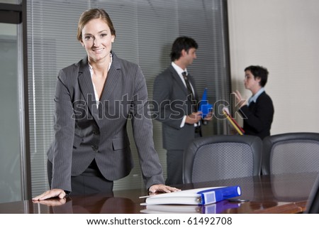 Confident business woman standing in boardroom, colleagues meeting in background