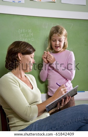 Back to school - 8 year old student and teacher by blackboard in classroom