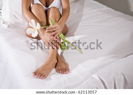 Low section of sexy woman with beautiful legs holding flower sitting on white bedspread