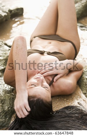 High angle view of beautiful young woman in bikini laying on rocky beach