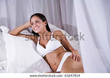 Sexy beautiful young Hispanic woman sitting on white canopy bed
