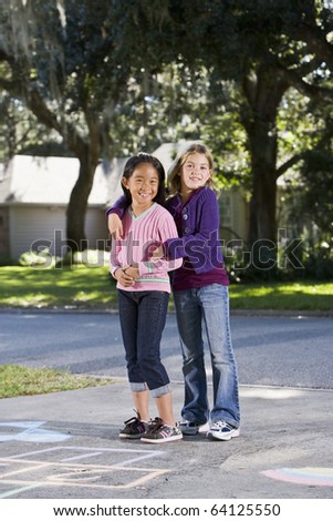 Two girls at home on driveway standing in front of hopscotch board (7 years)