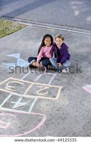 Two girls, 7 years, sitting in front of hopscotch board and other chalk drawings