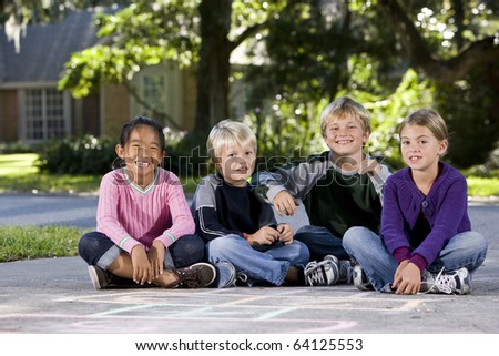 Four kids ages 7 to 9 sitting together in a row on driveway outside house