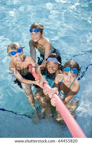 Multiracial friends tugging on pool toy in swimming pool, ages 7 to 9