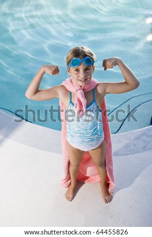 Girl, 7 years, playing by swimming pool in pretend superhero costume flexing muscles