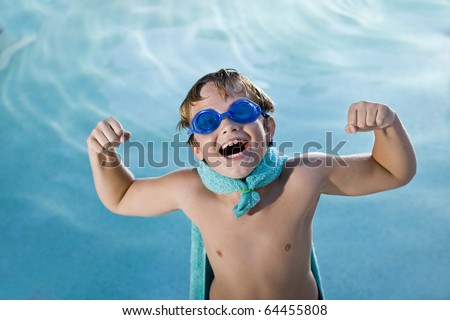 Boy, 9 years, playing by swimming pool in pretend superhero costume flexing muscles