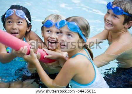 Four kids (7 to 9 years) playing tug of war with pool toy, girl in foreground not in focus
