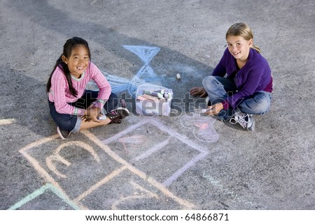 Two girls, 7 years, drawing pictures on driveway with chalk