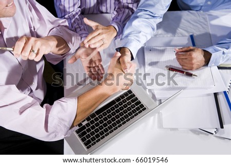 Three office workers working together on project, shaking hands and clapping.  Finished project or solved a problem.