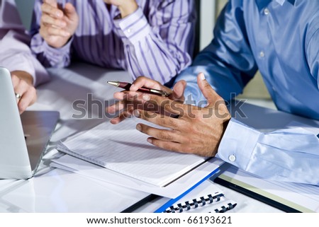 Three office workers working together on project, gesturing, focus on hand in middle