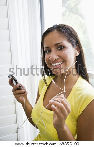 Hispanic woman listening to music on mp3 player by window at home