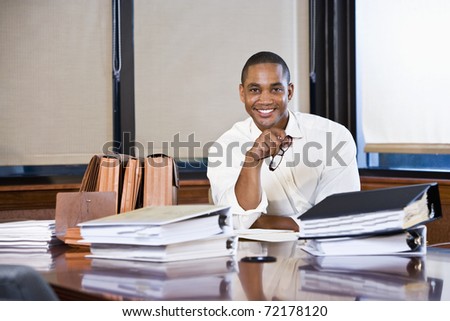African American office worker with stacks of documents on table in boardroom