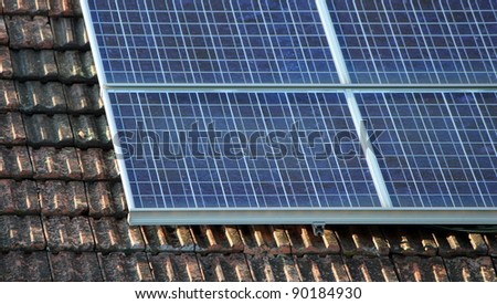Several solar panels on an old roof made of brown tiles