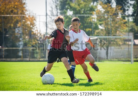 Boys Kicking Football On The Sports Field