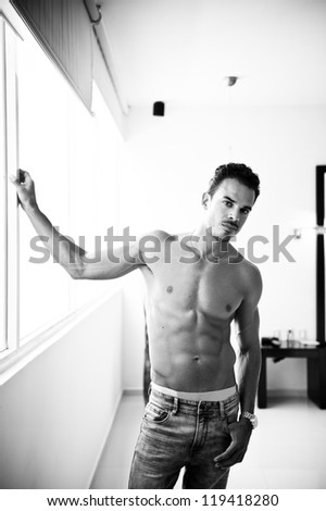 Portrait of a thoughtful handsome shirtless young man looking out of a window