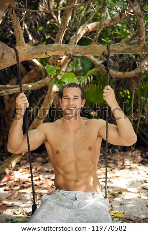 Attractive man sitting on a swing in the middle of the jungle