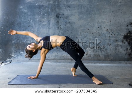Woman practicing advanced yoga against a dark texturized wall