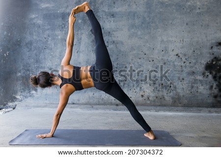 Woman practicing advanced yoga against a dark texturized wall