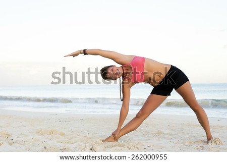 Woman practicing yoga at the beach - triangle pose