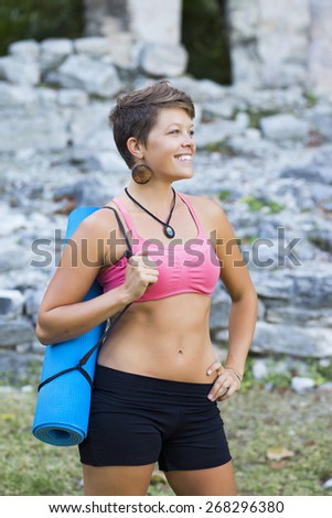 Woman with short hair and yoga mat outdoors looking happy and confident