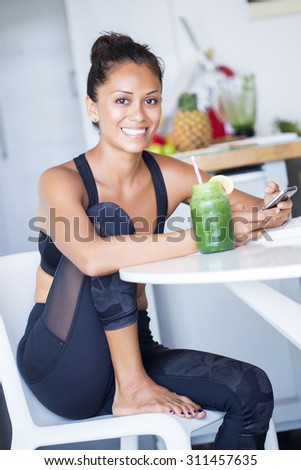 Woman drinking a homemade green detox juice, wearing sportive clothing.